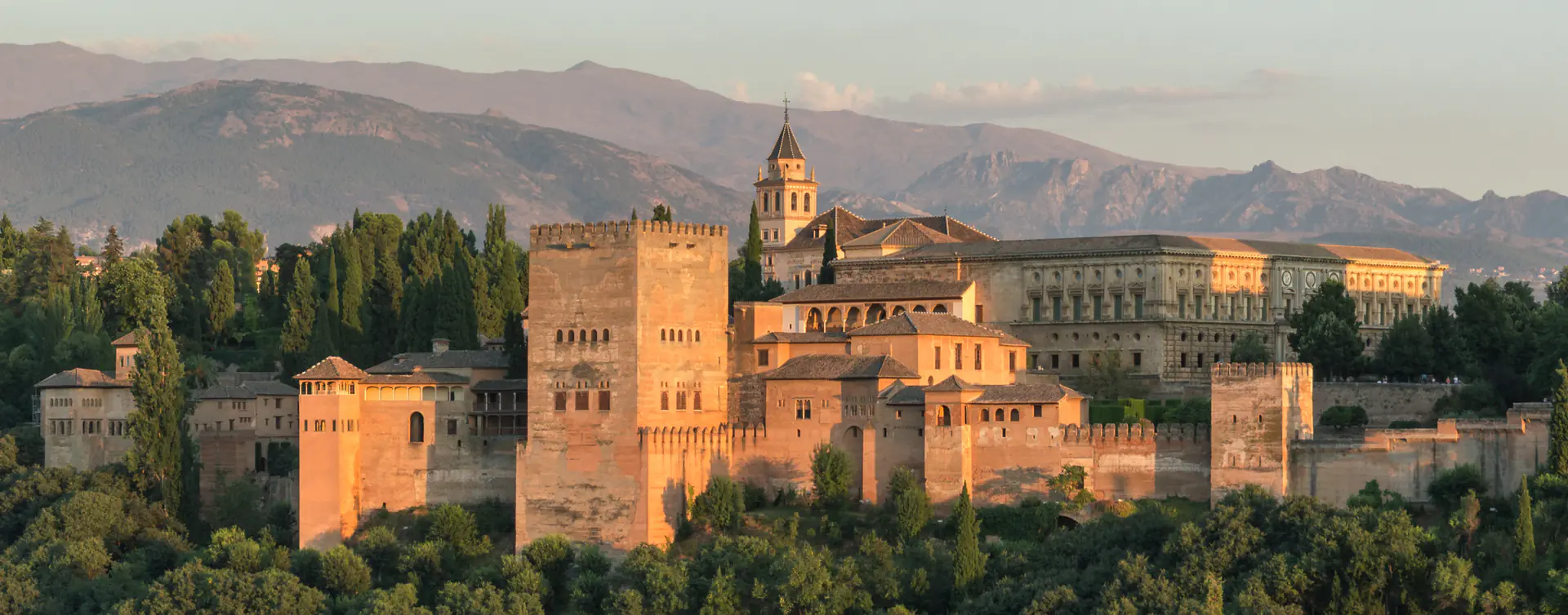 Panoramic evening view of Alhambra palace complex with Sierra Nevada mountains backdrop in Granada, Spain
