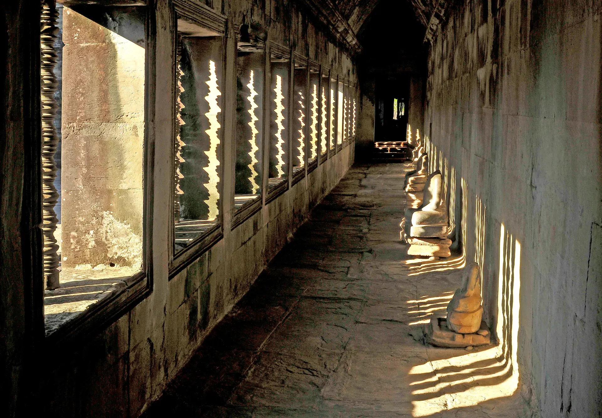 Stone corridor within Angkor temple showing the covered gallery architecture with columns and carved doorways creating dramatic perspective