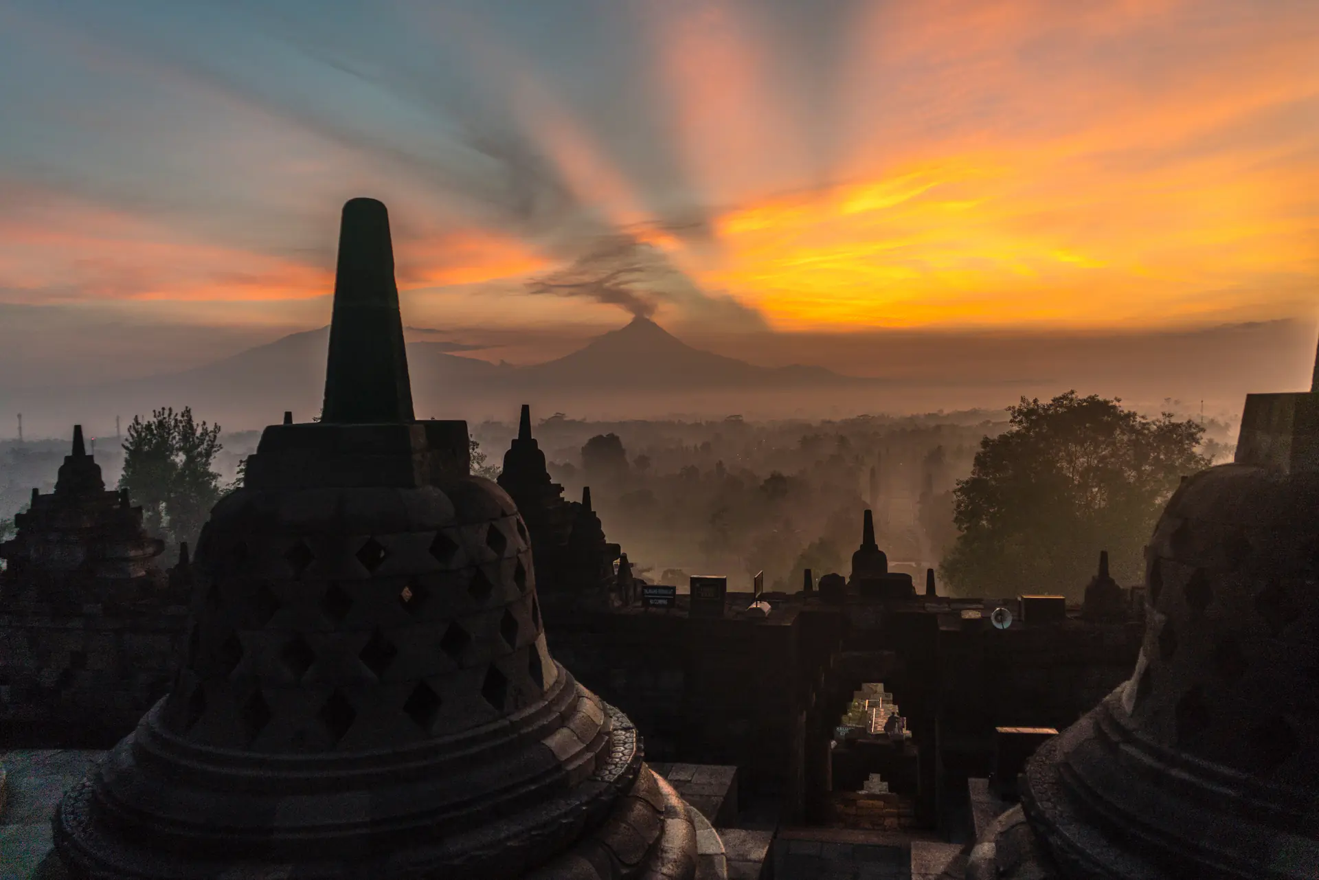 Amanecer en el Templo de Borobudur con luz dorada iluminando estupas en forma de campana y montañas volcánicas visibles a través de la niebla matutina