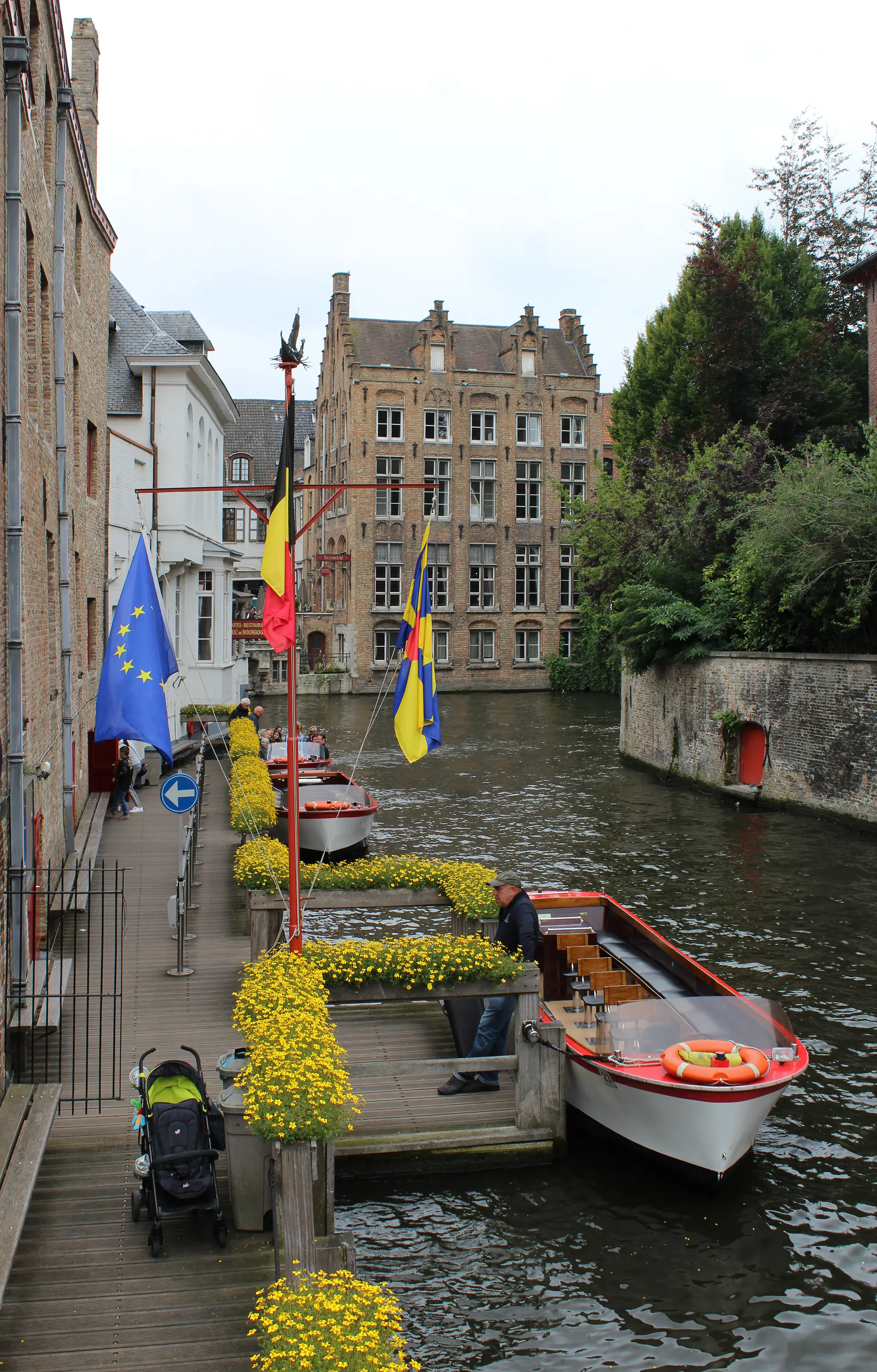 Traditional canal boat tour on Bruges waterway with medieval buildings, stone bridges, and tourists experiencing the Venice of the North