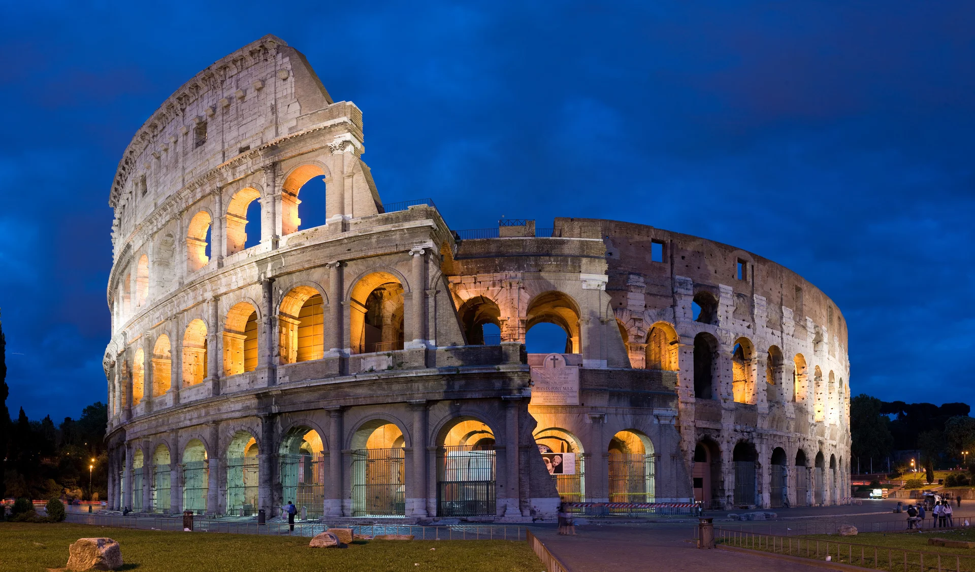 The iconic Colosseum (Flavian Amphitheatre) in Rome showing its massive elliptical structure with multiple arched tiers against the blue Italian sky