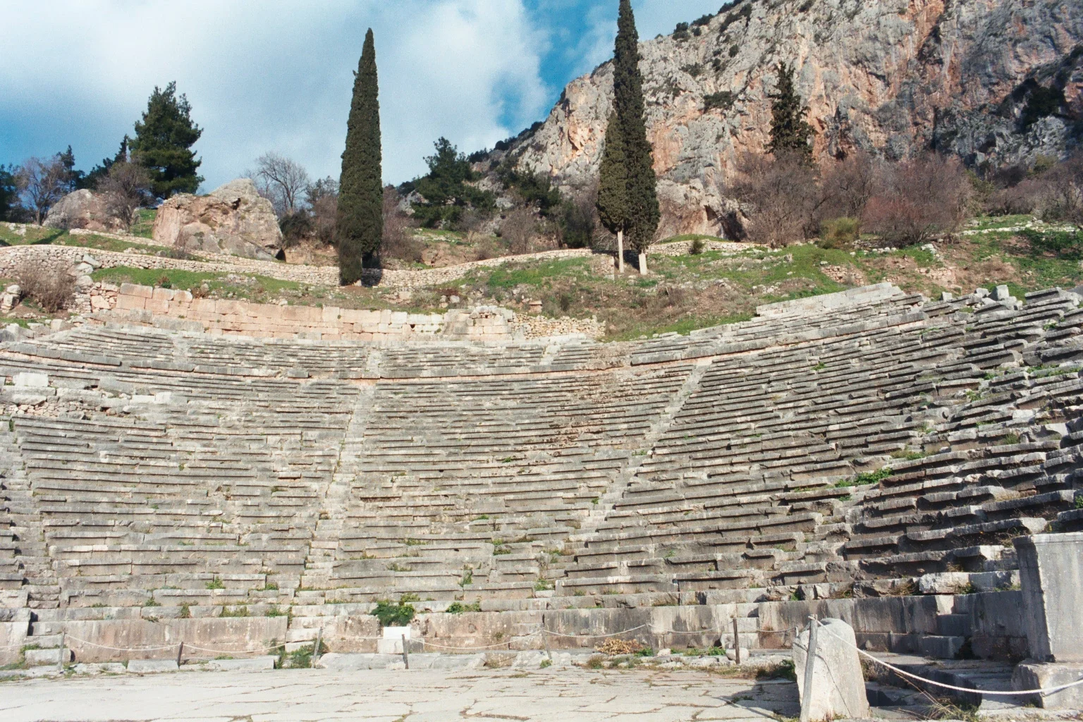 The ancient Greek theatre at Delphi showing curved stone seating rows carved into the hillside with mountain views beyond