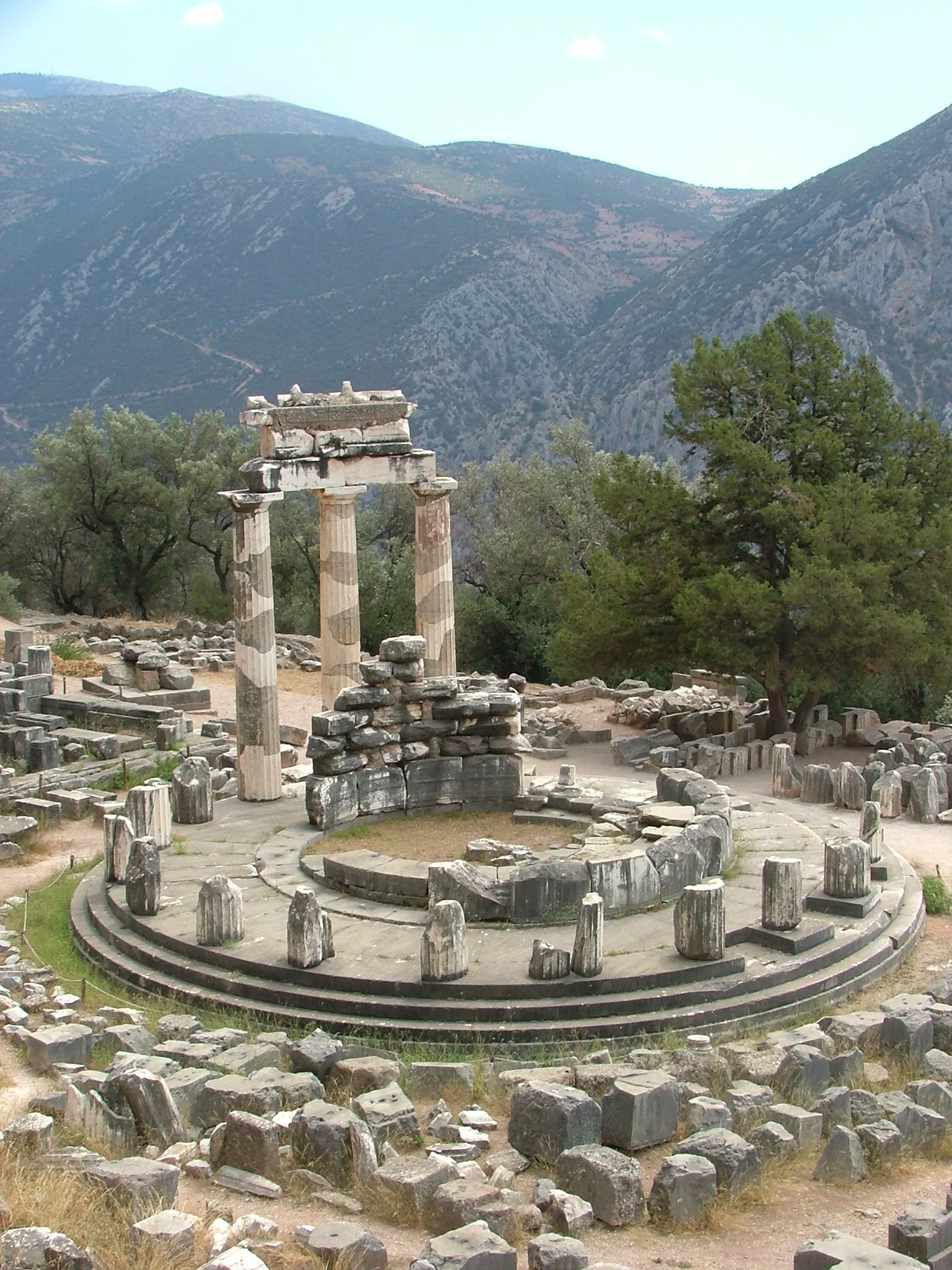 The ancient Tholos at Delphi showing three restored Doric columns of the circular temple with mountain landscape in the background
