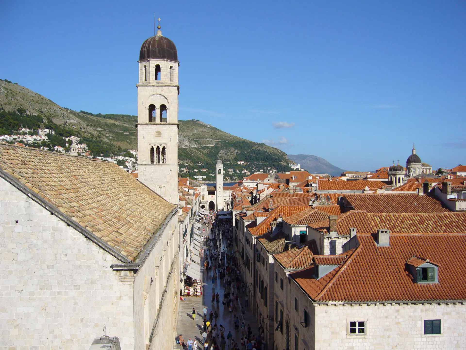 La calle principal Stradun de Dubrovnik con pavimento de piedra caliza pulida, fachadas de edificios barrocos y la Torre del Reloj visible al extremo oriental