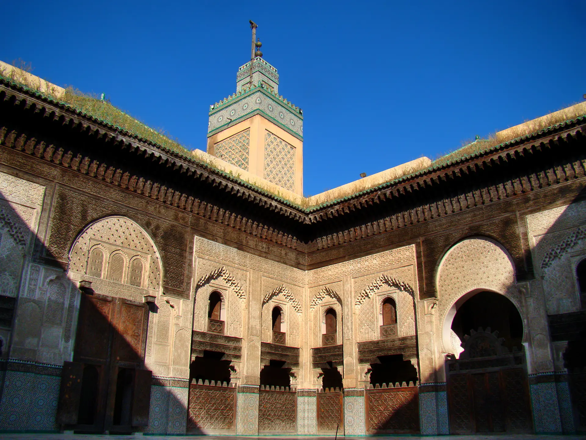 Patio interior de la Madrasa Bou Inania mostrando intrincados patrones geométricos islámicos, trabajo de zellige, estuco tallado y ornamentado trabajo en madera de cedro