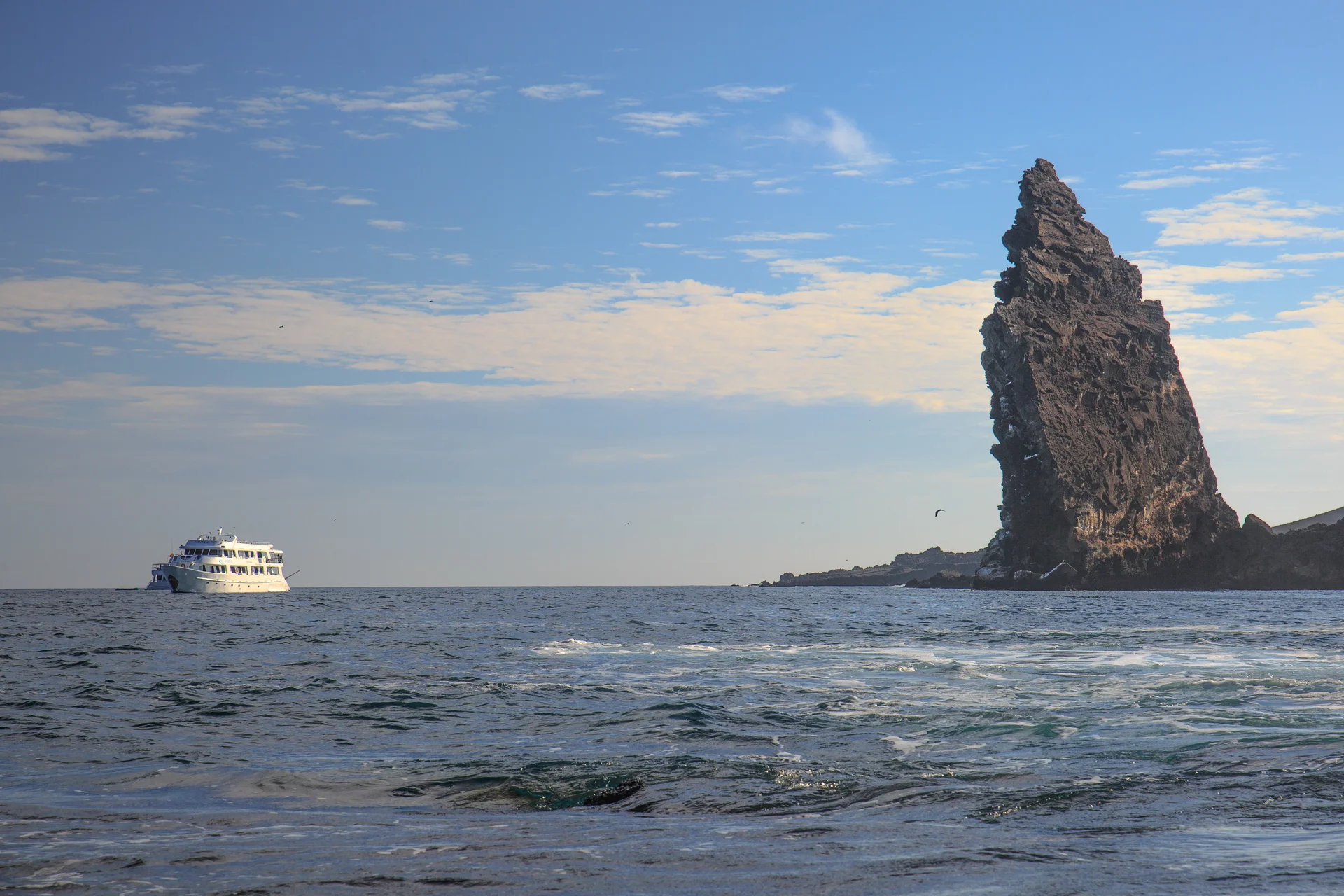 The iconic Pinnacle Rock volcanic formation on Bartolomé Island with Santiago Island's dark lava flows in the background under clear blue skies