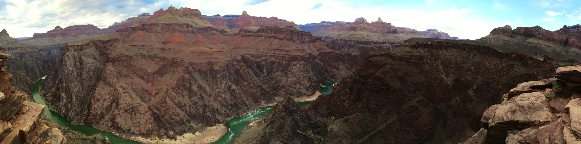 Panoramic view of Colorado River winding through deep Grand Canyon inner gorge with towering rock walls demonstrating ongoing erosional processes
