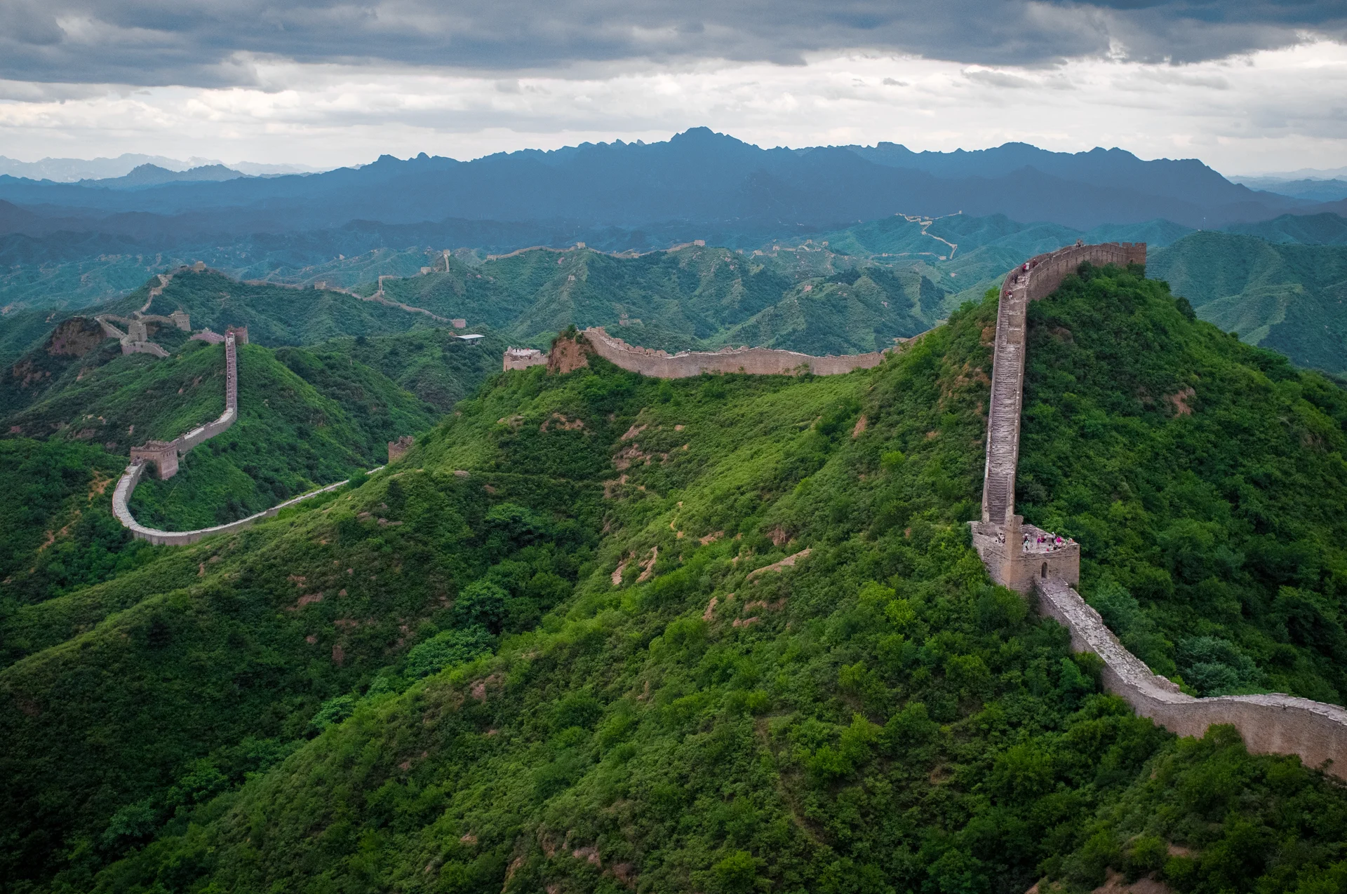 Jinshanling section of the Great Wall showing dramatic unrestored fortifications winding along mountain ridges with multiple watchtowers in atmospheric lighting