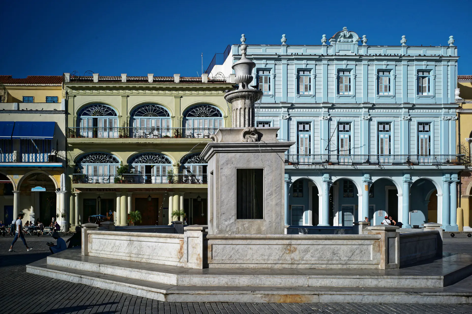 Colorful colonial buildings surrounding Plaza Vieja in Old Havana, showing the restored baroque and Art Nouveau facades with their distinctive arcades and balconies