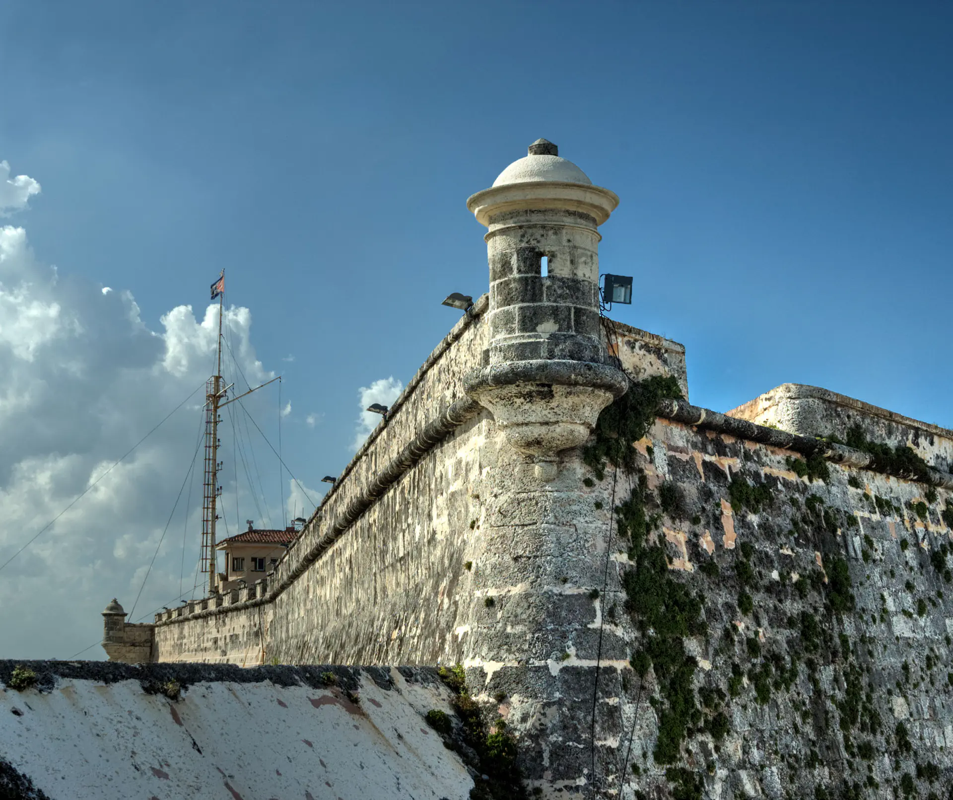 Morro Castle fortress with its iconic lighthouse perched on rocky cliffs overlooking the entrance to Havana harbor, with waves crashing against the stone fortifications