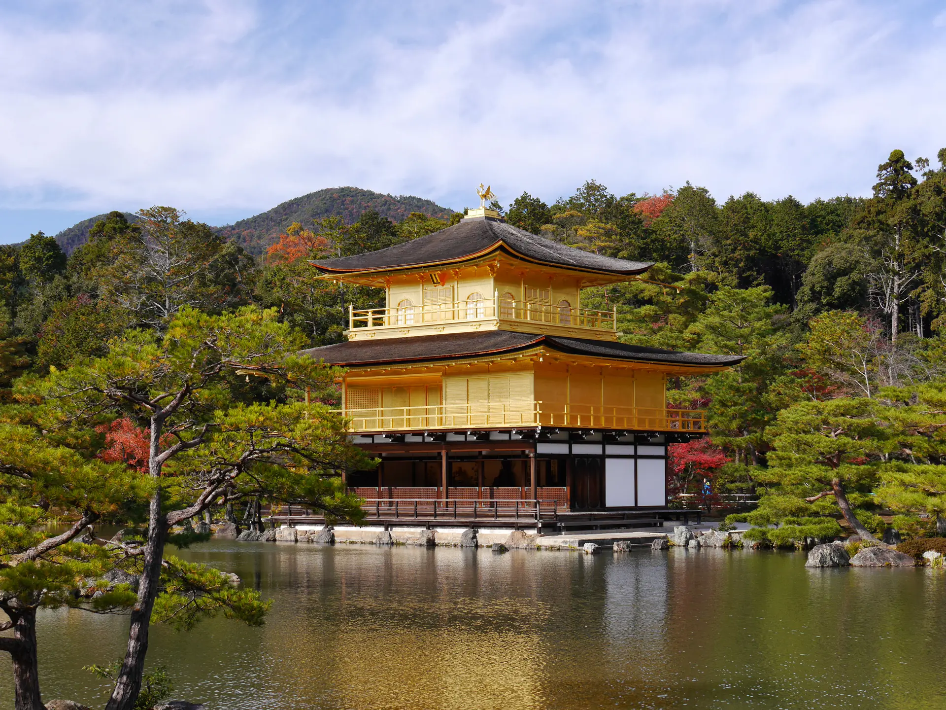 The spectacular Kinkaku-ji Golden Pavilion reflecting in Mirror Pond, with its gold-leaf-covered upper stories gleaming against the backdrop of Japanese garden and forested hills