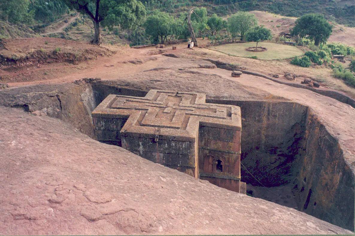 Bet Giyorgis church viewed from above showing the perfectly carved Greek cross shape in red volcanic rock with pilgrims descending the steep pathway into the trench