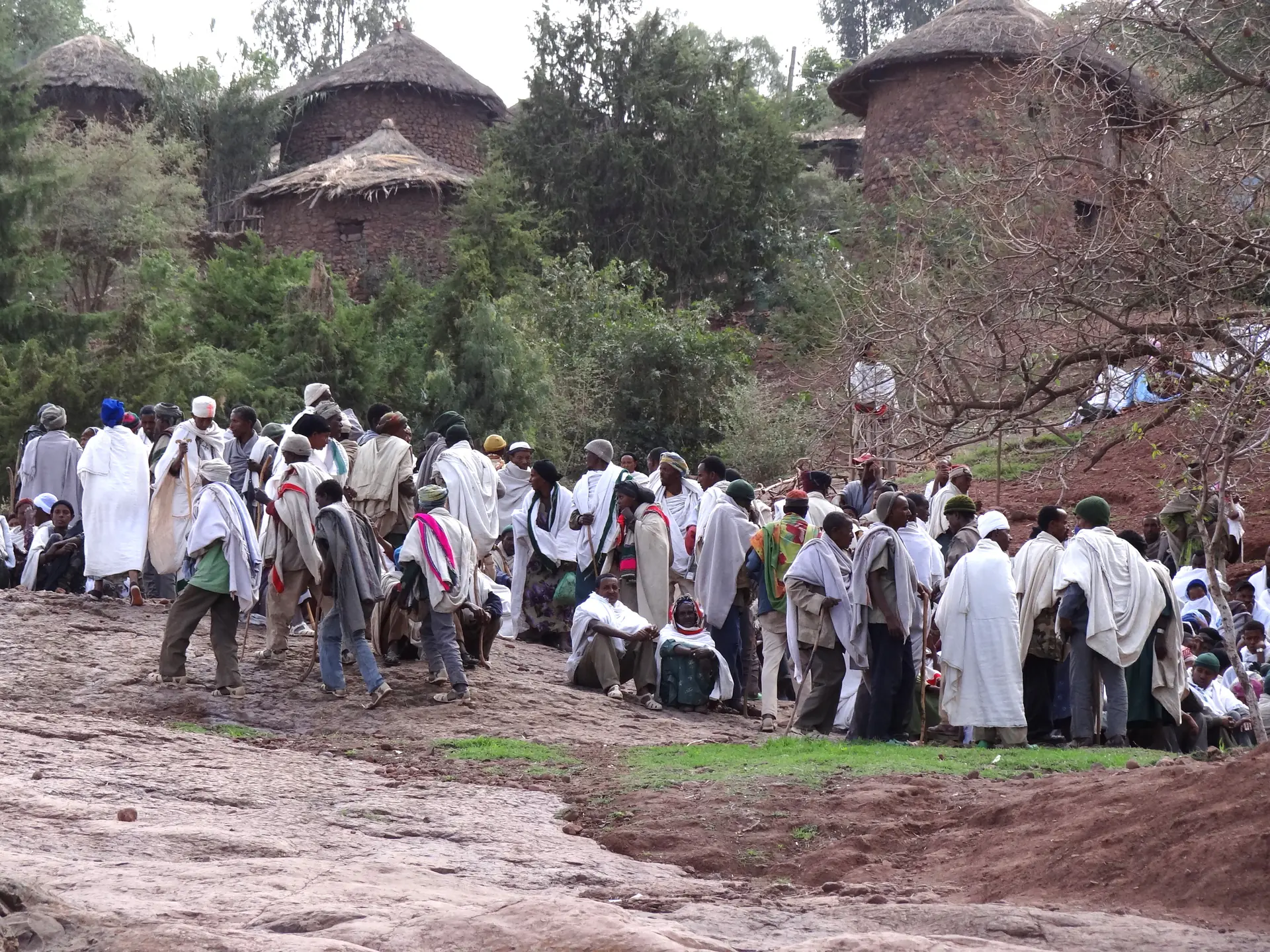 Ethiopian Orthodox pilgrims dressed in traditional white robes gathered around Bet Giyorgis church during a major religious festival, with priests visible at the church entrance