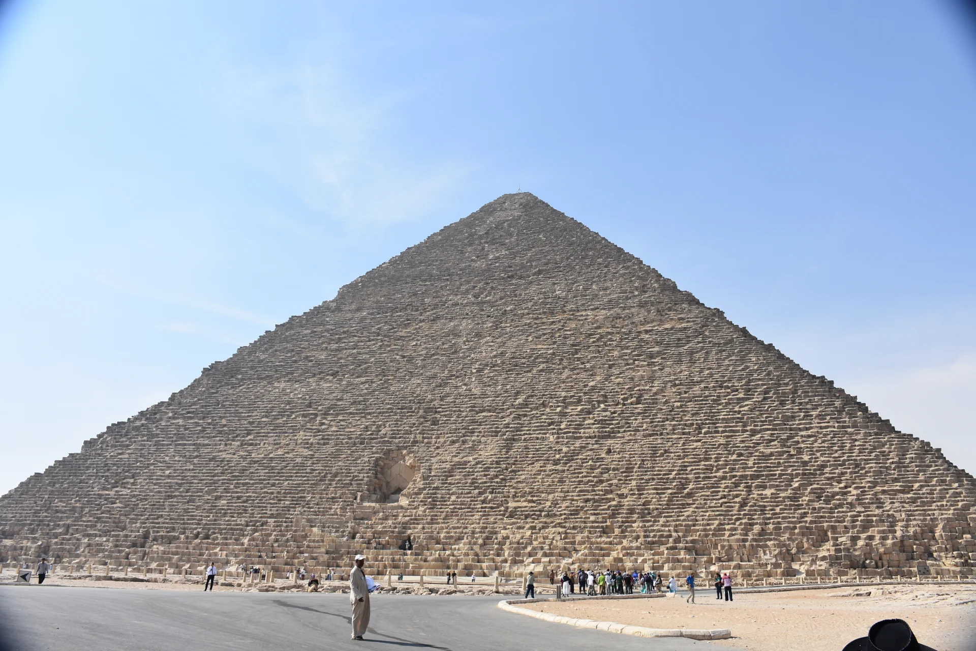 The Great Pyramid of Khufu rising majestically against the blue sky, showing the massive limestone blocks and original smooth casing stones at the apex