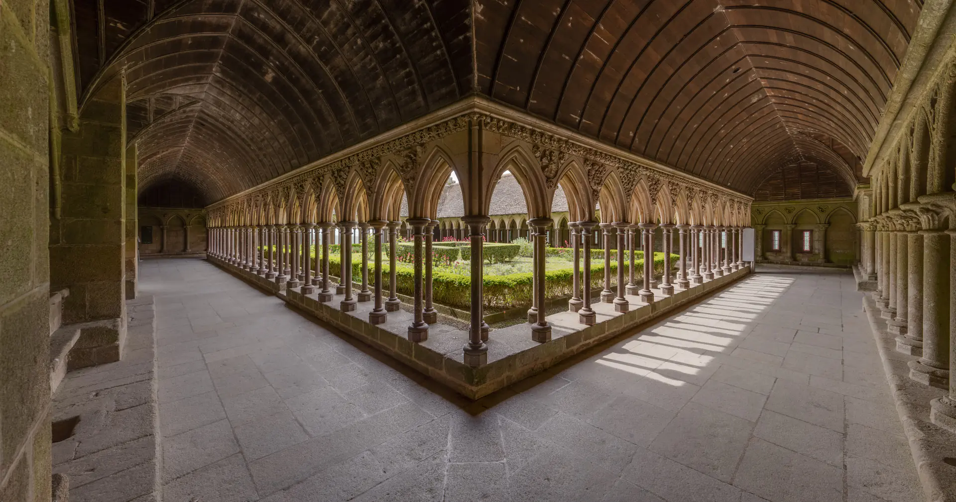 Stunning panoramic view of La Merveille cloister showing the complete Gothic colonnade with staggered columns in quincunx pattern, arched walkways, and serene garden courtyard
