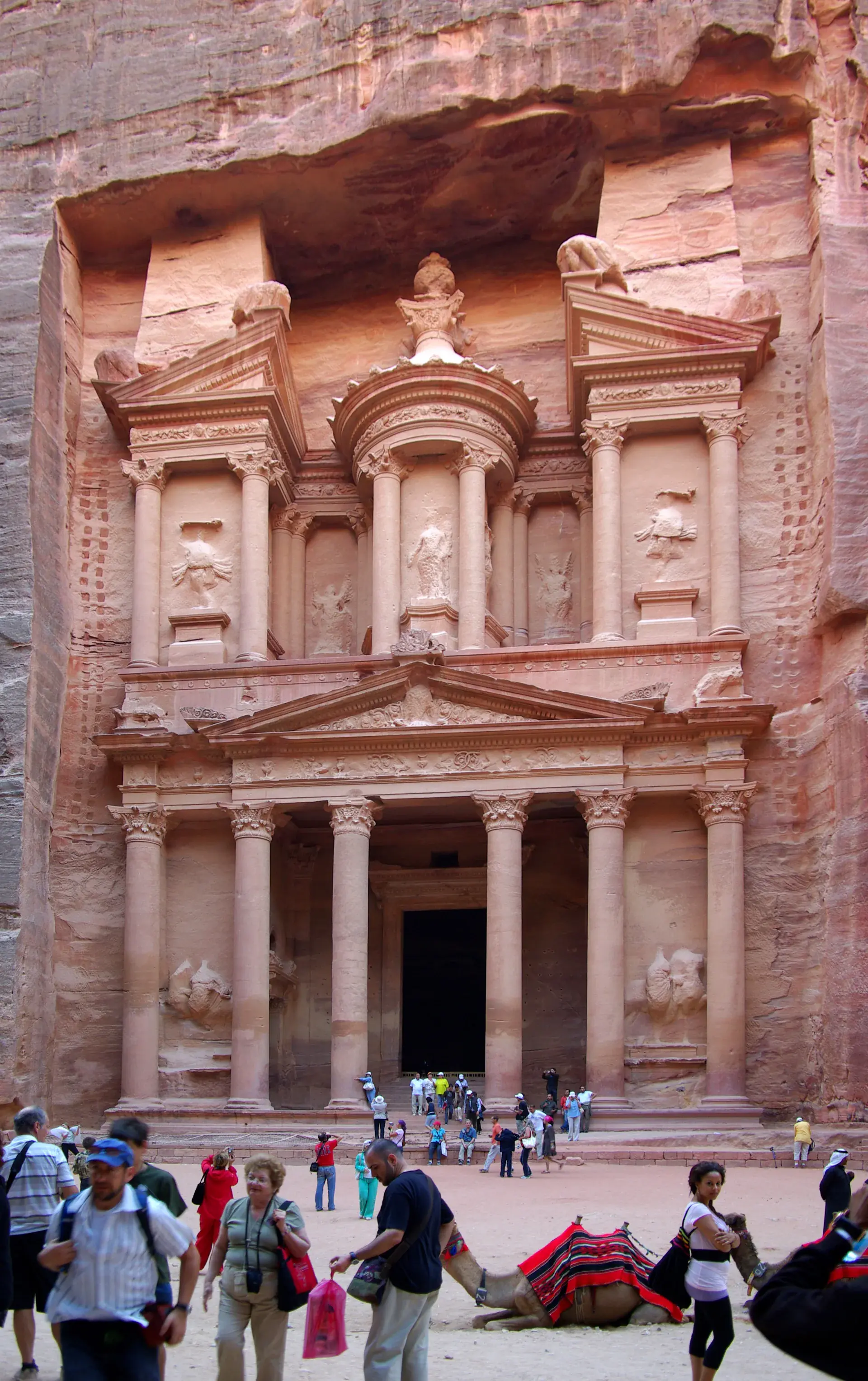 The iconic Treasury (Al-Khazneh) of Petra carved into rose-red sandstone cliff face, showing intricate Nabataean architecture with classical columns and ornate details