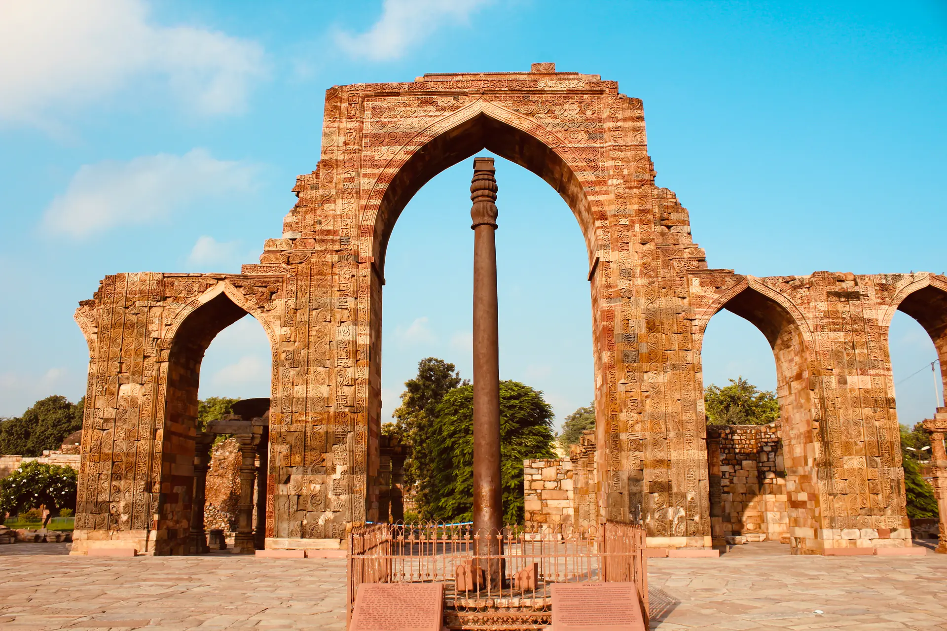 The ancient rust-resistant Iron Pillar standing in the Qutb Complex courtyard showing Sanskrit inscriptions and remarkable preservation after 1,600 years