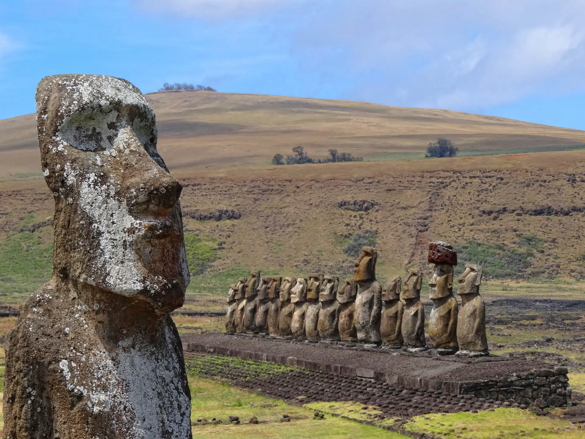 The iconic Traveling Moai statue in foreground with the fifteen Ahu Tongariki moai standing in formation against the Easter Island landscape