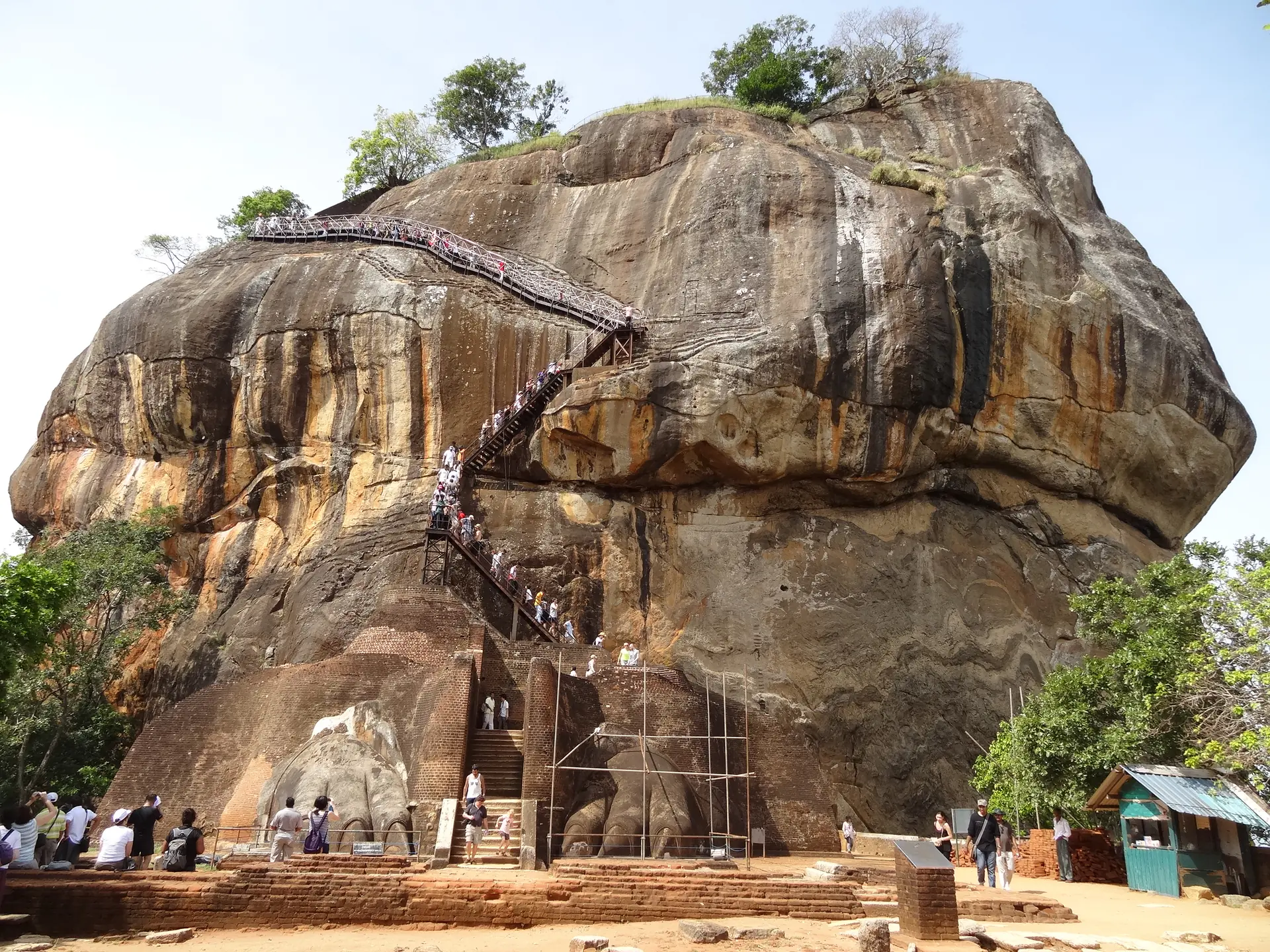 Enormes patas de león talladas en Sigiriya marcando la entrada al ascenso final del palacio con escaleras empinadas visibles detrás
