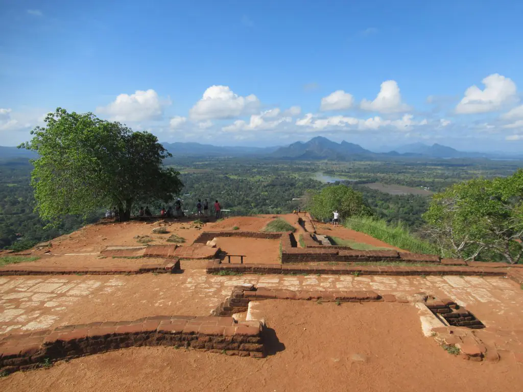 Antiguas ruinas del palacio y cisternas talladas en roca en la meseta de la cumbre de Sigiriya con visitantes explorando los restos arqueológicos