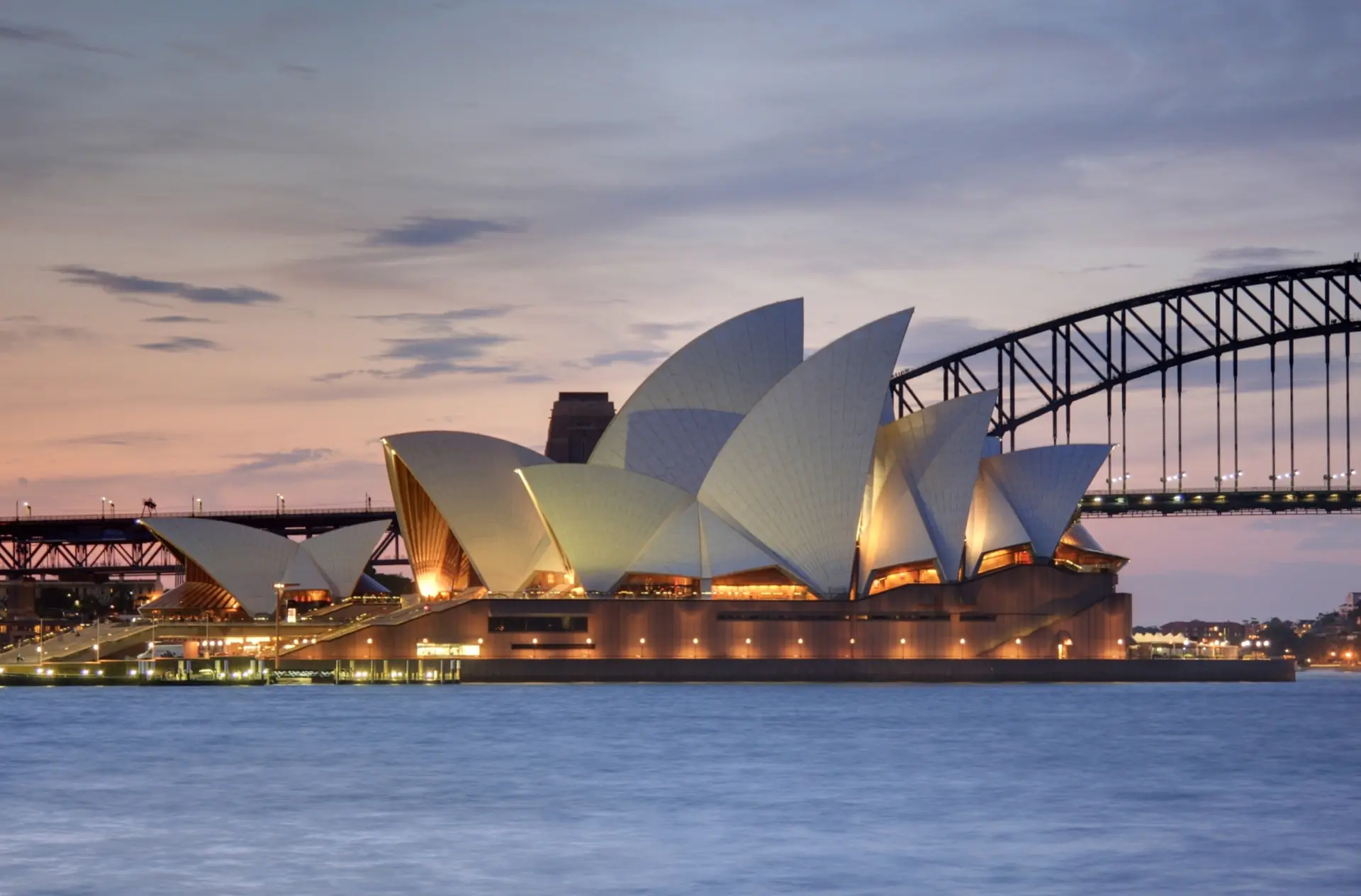 Sydney Opera House iconic white shell structures viewed from Royal Botanic Gardens with harbour waters and palm trees in foreground