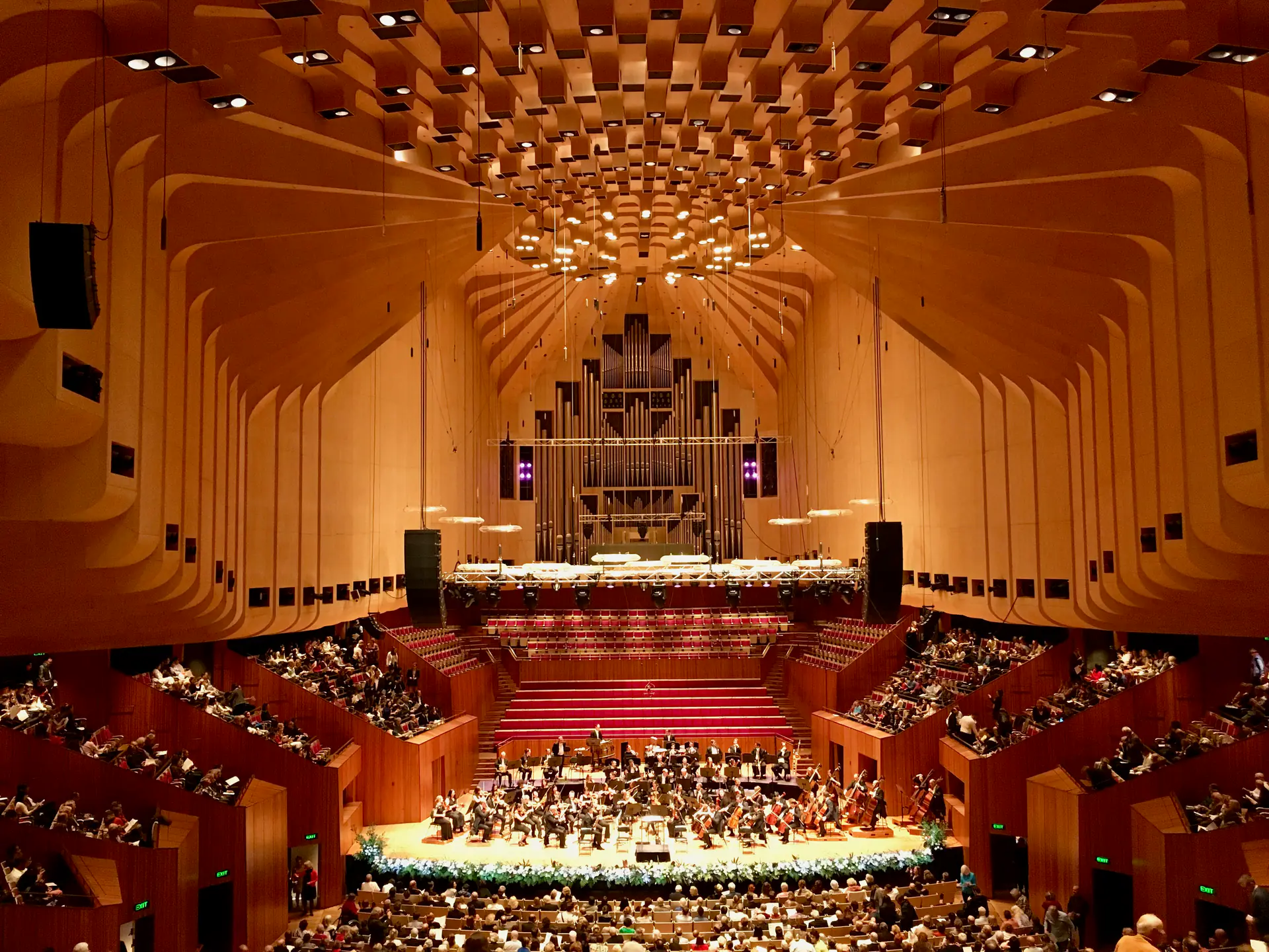 Interior of Sydney Opera House Concert Hall during live performance showing audience, stage, and acoustic reflectors