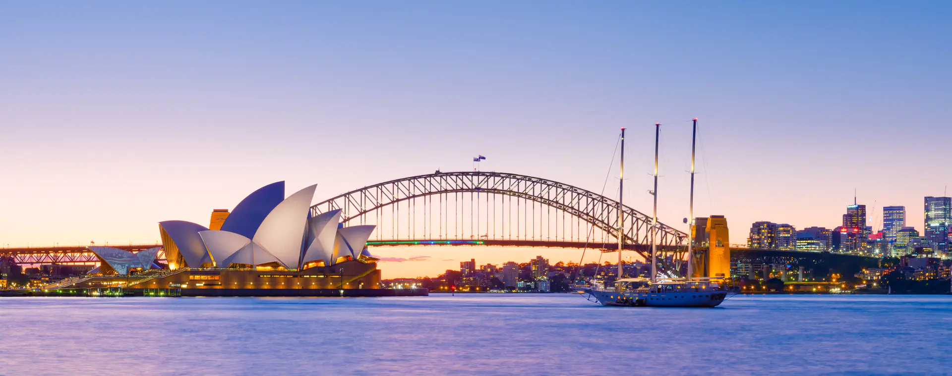 Sydney Opera House and Harbour Bridge at dusk with colourful sunset sky reflected in harbour waters