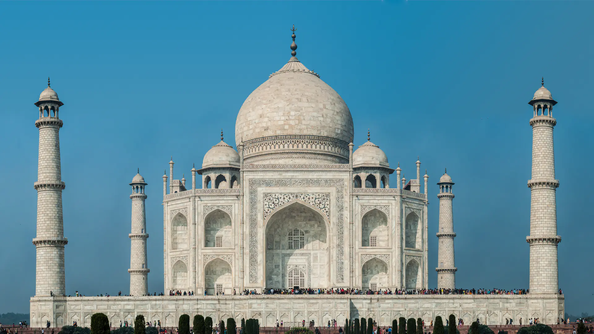 The iconic white marble Taj Mahal mausoleum with its central dome and four minarets reflected in the long rectangular pool