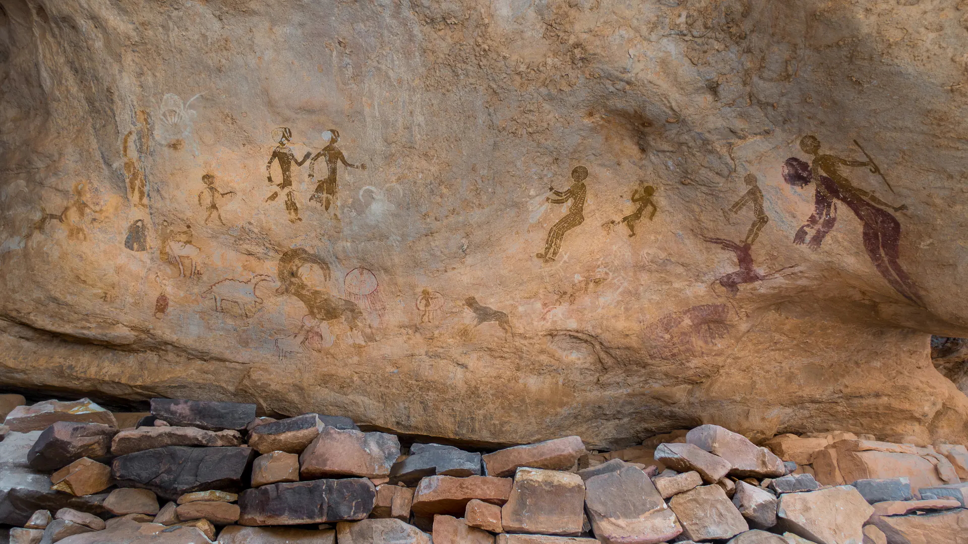 Ancient Neolithic cave painting from Tanzoumaitak in Tassili n'Ajjer showing prehistoric figures and animals in ochre pigments on rock surface