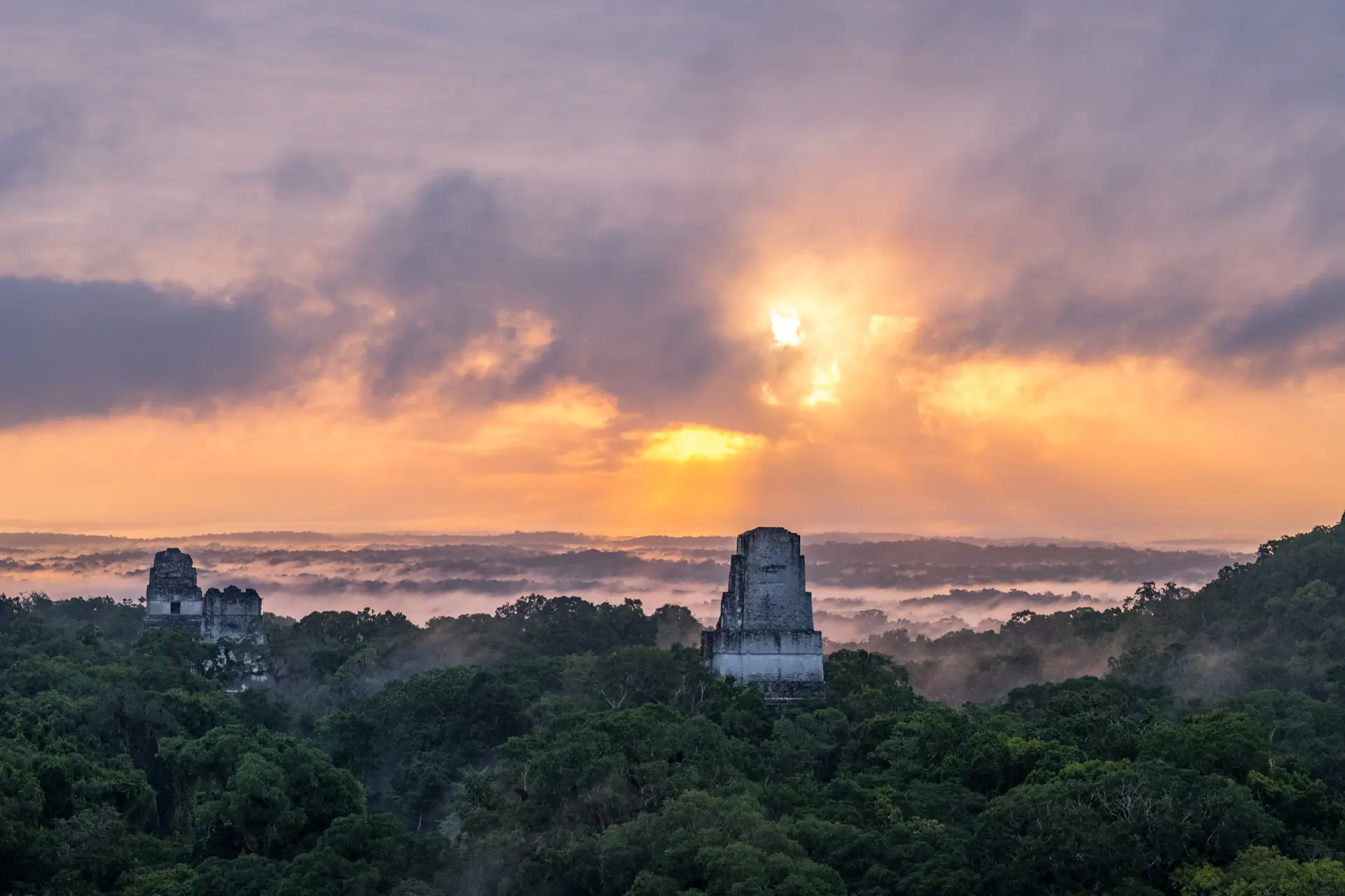 Amanecer sobre los antiguos templos mayas en el Parque Nacional Tikal en la región de Petén, Guatemala, mostrando el dosel brumoso de la selva y las icónicas estructuras piramidales