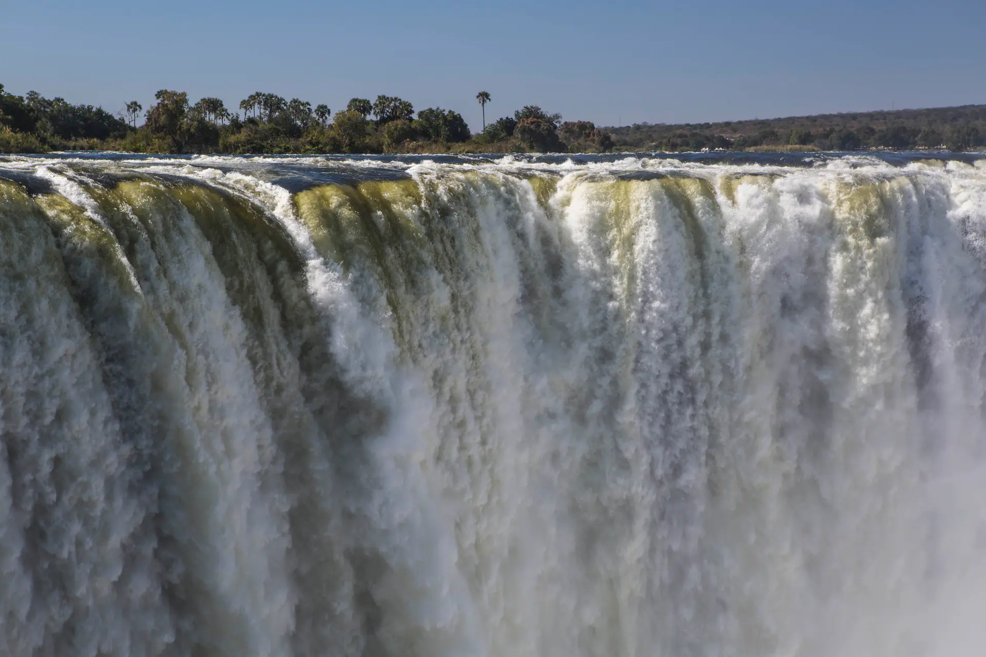 Dramatic view of Victoria Falls from Zimbabwe viewpoint showing massive water curtain plunging into gorge with towering mist spray