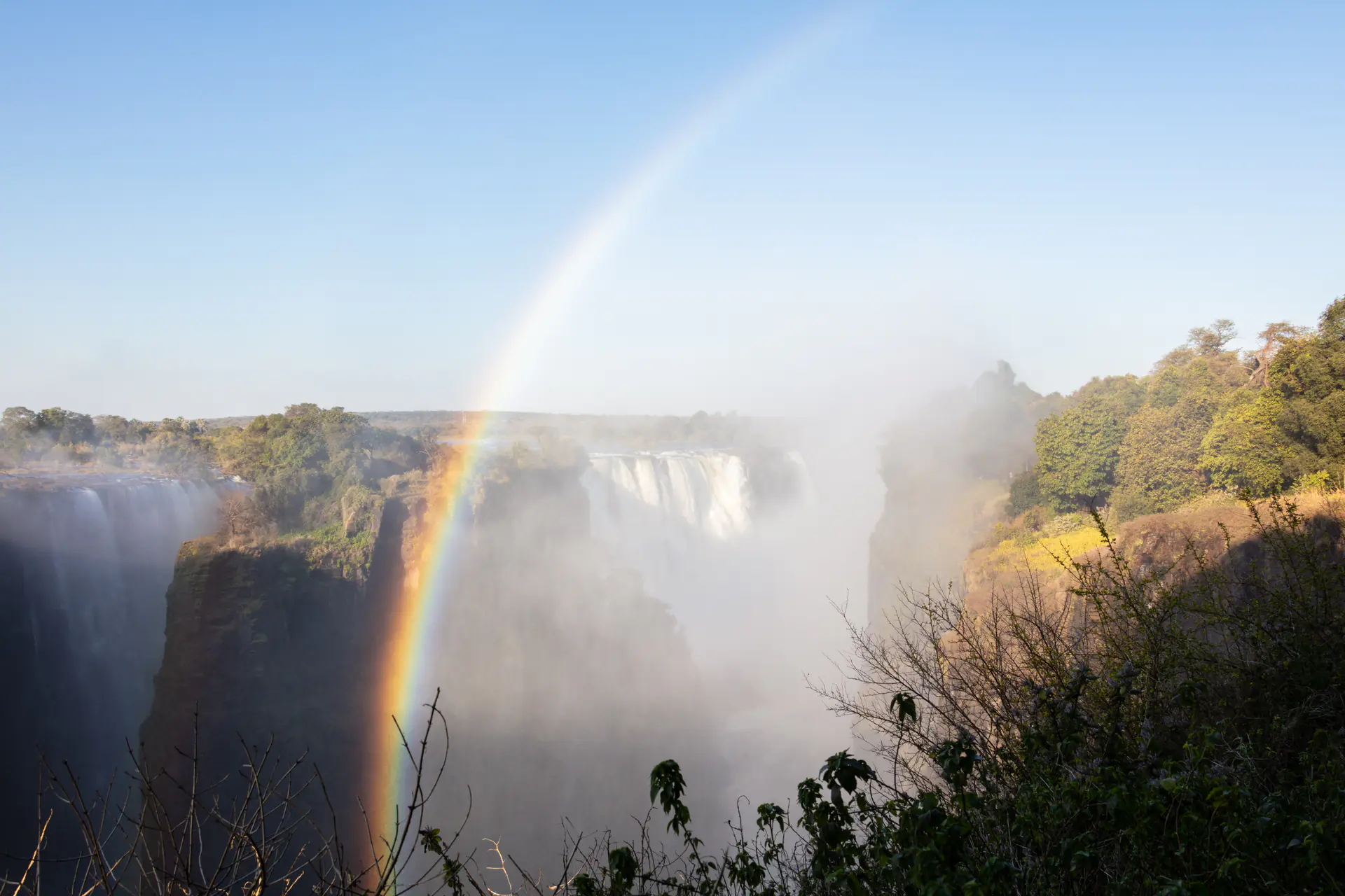 Vibrant rainbow arcing across Victoria Falls with waterfall spray illuminated by sunlight