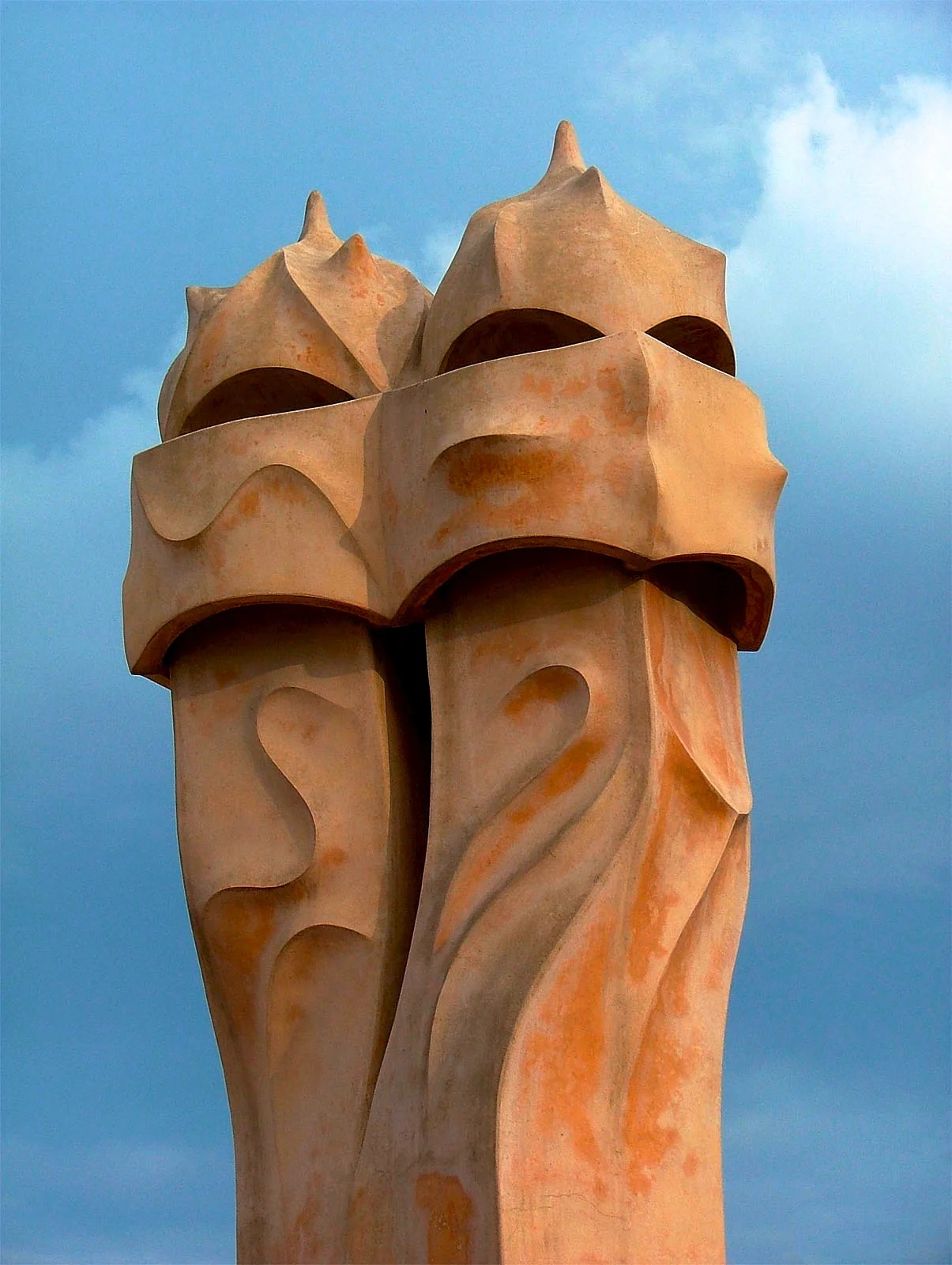 Sculptural chimneys and ventilation towers on Casa Milà rooftop with Barcelona skyline in background showing Gaudí's innovative architectural approach